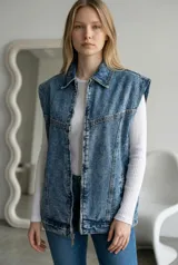 Chaleco de jean con efecto lavado ácido, corte oversize, cuello camisero y cierre frontal con cremallera metálica.