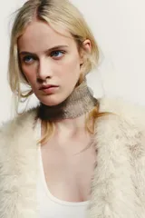 Chaleco Zara de pelo sintético en color beige, con diseño abierto, manga muy corta y cierre lateral con clip.