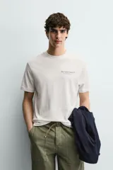 Camiseta de corte relajado, color blanco, con cuello redondo y manga corta. Presenta un pequeño estampado en el pecho con texto y un diseño gráfico más grande en la espalda.