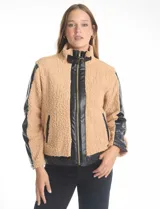Campera de corderito sintético color beige con paneles y detalles en cuero sintético negro. Presenta cuello alto con tira y hebilla metálica, cierre frontal metálico y mangas largas con paneles de cuero sintético.