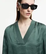Blusa de manga larga color verde oscuro con acabado satinado y escote en V con solapa ancha.