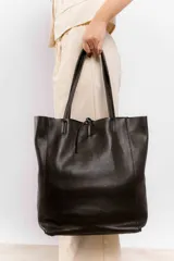 Bolso tote grande de cuero negro con doble asa larga y cierre superior con tira de cuero. Diseño minimalista y atemporal.
