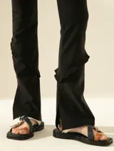 Pantalón negro elastizado de calce ajustado, con cintura elástica y cierre lateral. Presenta volados y tajos en las botamangas.