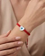 Pulsera de hilo rojo en macramé con dije en forma de corazón de nácar con diseño de ojo turco. Cuenta con cierre regulable con esferas plateadas en las terminaciones.