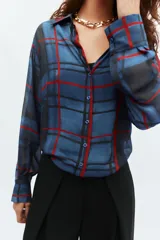 Camisa de manga larga con cuello solapa y cierre frontal con botones. Presenta un diseño de cuadros en tonos azules y rojos sobre un tejido semitransparente.