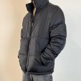 Campera puffer color gris claro, con cuello alto y cierre frontal con cremallera.