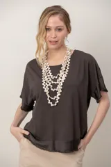 Remera verde oscuro de algodón, con cuello redondo, mangas cortas y zócalo de satén desflecado en el ruedo y las mangas.
