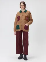 Campera tejida de punto grueso en color beige, con cuello en contraste color verde. Presenta cierre frontal con botones, bolsillos delanteros con apliques en nylon color marrón y bordado decorativo, y forro interno de nylon.