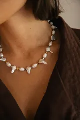 Collar corto de perlas de río y perlas barrocas con formas irregulares, intercaladas con pequeñas piezas metálicas en tonos dorado y plateado. Cuenta con cadena de extensión para regular el largo.