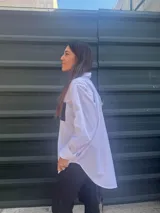 Camisa blanca de corte clásico con bordado de hilo negro en el hombro y bolsillo de cuerina negro en el pecho.