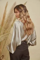 Blusa de satén con cuello a la base, mangas anchas tipo murciélago y puños elásticos con detalles bordados.