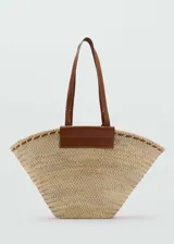 Bolso tipo capazo de gran tamaño, confeccionado en fibra natural trenzada con detalles de cuero marrón en las asas y en la parte superior.