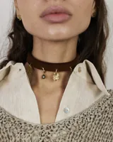 Gargantilla tipo choker de gamuza con dijes colgantes artesanales de metal y perlas naturales. Cuenta con tiras largas para atar y ajustar en la parte posterior.