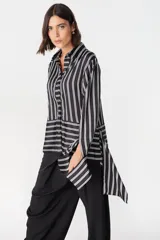 Camisa de corte holgado con estampado de cuadros en tonos marrones y beige. Presenta cuello clásico, cierre frontal con botones y mangas largas con aberturas laterales que permiten anudar la prenda en la cintura.