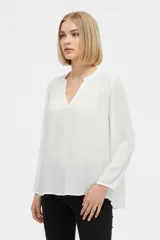 Blusa blanca de viscosa con detalles de broderie en los hombros, cuello en V y mangas largas holgadas.