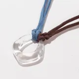 Collar con colgante de vidrio transparente en forma de gota irregular, con cordón doble de gamuza sintética color celeste y marrón.