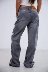 Jean de corte recto y tiro medio-bajo, color gris lavado, con detalle de estrellas bordadas a lo largo de los laterales externos de las piernas.