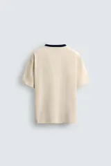 Camiseta de manga corta y cuello redondo, color azul marino, con ribete de contraste en color crema alrededor del cuello.