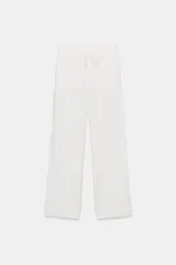 Pantalón blanco de tiro medio con pierna ancha y tejido que contiene lino. Presenta cintura con trabillas y un cinturón ajustable con lazada del mismo tejido. Cierre frontal con cremallera y botón.
