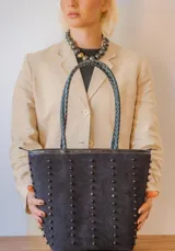 Cartera tipo tote de gamuza color marrón, con correas trenzadas y detalle de piedras naturales incrustadas en líneas verticales. Cuenta con cierre metálico y forro interior de tela.