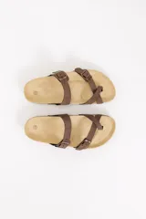 Sandalia marrón de diseño anatómico con dos tiras cruzadas que incluyen hebillas metálicas y una sujeción para el dedo. Cuenta con suela de corcho y base de goma antideslizante.