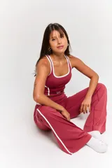Conjunto deportivo compuesto por un top corto y un pantalón largo, ambos de color bordó con detalles de líneas blancas en los costados. El top presenta cuello redondo y el logo 'bk.' estampado en el frente.