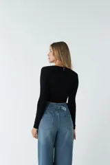 Top de manga larga en tejido rib negro, con escote en V profundo y detalle de nudo frontal que genera un efecto fruncido.