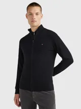 Cárdigan Tommy Hilfiger de color negro confeccionado en una mezcla de algodón pima orgánico y cachemira. Presenta un diseño con cierre de cremallera frontal, cuello levantado de punto canalé y el logo de la marca bordado en el pecho.