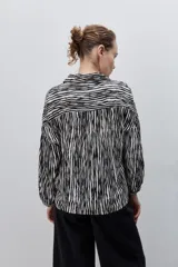 Camisa de calce amplio confeccionada en viscosa fluida con estampado animal print tipo cebra en blanco y negro. Presenta cuello camisero, escote en V y mangas largas con puños elastizados, además de frunces en el canesú que aportan volumen.