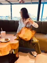 Bolso tote color marrón claro con textura símil piel de cocodrilo. Tiene doble asa corta, laterales de gamuza con flecos y un aplique floral en el frente.