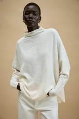 Jersey de punto con textura, color tostado, de cuello subido y manga larga. Presenta un diseño holgado con bajo asimétrico y aberturas laterales.