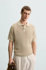 Polo de manga corta, color beige claro, con cuello solapa y cierre frontal de dos botones. Tejido de punto con textura acanalada vertical.
