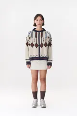 Campera tipo bomber tejida con diseño jacquard geométrico en tonos azul marino, blanco, rojo y verde. Presenta cierre frontal completo, cuello, puños y ruedo acanalados en color verde y blanco, con corte oversized y hombros caídos.