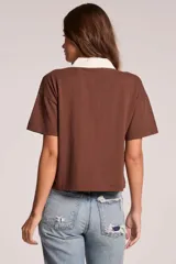 Remera de manga corta color marrón con cuello polo y solapa frontal con botones en color blanco contrastante, de corte recto y holgado.