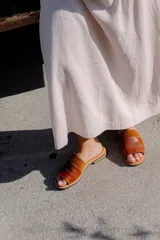 Sandalias planas de cuero marrón con tira ancha sobre el empeine. La plantilla es de cuero con la inscripción "LE".