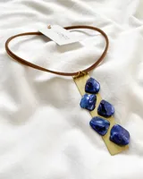Collar con tiento de cuero marrón, dije rectangular de metal dorado y piedras de color azul.