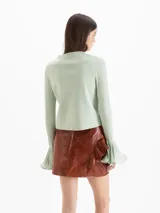 Minifalda de cuero ovino color marrón, de tiro medio-alto y silueta entallada. Presenta un recorte diagonal con un volado aplicado de forma asimétrica.