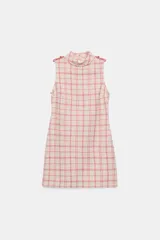 Vestido corto sin mangas de tejido texturizado con diseño de cuadros en tonos crudo y fucsia. Presenta cuello subido, trabillas decorativas con botones dorados en los hombros y cierre lateral con cremallera oculta.