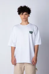 Remera de corte oversize color blanco, con cuello redondo y mangas cortas. Presenta un pequeño logo estampado en el pecho y un diseño gráfico grande en la espalda que incluye la frase 'Good Children' e ilustraciones de un ángel y llamas.