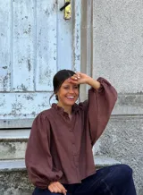 Camisa de lino color marrón, de corte holgado, con cuello elevado con volado sutil y mangas abullonadas con puños elásticos. Cierre frontal con botones.