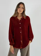 Camisa color ladrillo de terciopelo de viscosa con cuello clásico, cierre frontal con botones y mangas largas con puños elásticos.