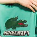 Remera verde con estampado del logo de Lacoste pixelado al estilo Minecraft y el logo de Minecraft debajo.