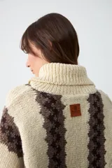 Sweater de punto grueso con cuello tortuga, diseño de rayas verticales en color crudo y marrón, de corte holgado y manga larga.
