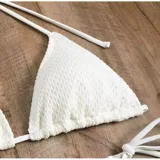 Conjunto de baño de cuatro piezas en color negro, confeccionado en tejido de malla transparente. Incluye un top de bikini triangular, una remera manga larga abierta con lazo frontal para anudar, y una pollera corta ajustable con cordones laterales.