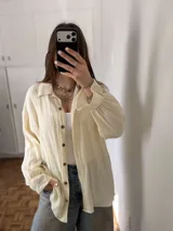 Sobrecamisa oversize de muselina color crudo, con cierre frontal de botones, mangas largas y puños fruncidos con volado.