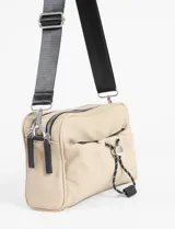 Bandolera color verde militar, confeccionada en material waterproof. Cuenta con doble cierre en el compartimento principal, un bolsillo frontal con cierre y cordón ajustable con stopper, y un bolsillo trasero con cierre. Incluye correa larga regulable de color negro.