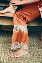 Pantalón de tiro medio confeccionado en tejido satinado, con cintura elástica y pernera recta. Presenta detalles de encaje y bordados en contraste en el ruedo.