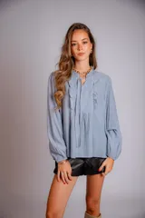 Camisa celeste con cuello con volados y lazos, mangas largas con puños elásticos y corte holgado.