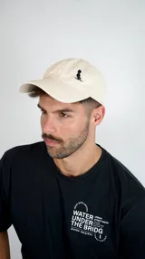 Gorra tipo dad hat color beige con bordado pequeño en color negro en el panel frontal.