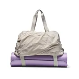 Bolso deportivo de gran capacidad con diseño arrugado, color gris claro. Cuenta con doble asa superior, correa ajustable y desmontable, y correas en la base para sujetar accesorios. Incluye compartimento principal con cierre, bolsillo frontal y bolsa interior desmontable.